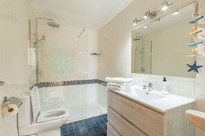 A modern bathroom with a glass-enclosed shower, a white sink with a mirror, and a wooden vanity. - Skyline Cala Nau by Rentallorca (Cala Millor)