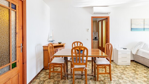 Un coin repas avec une table en bois, des chaises, un buffet blanc et un lit.