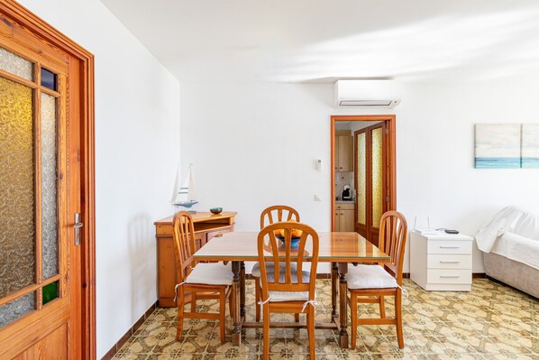Un coin repas avec une table en bois, des chaises, un buffet blanc et un lit.