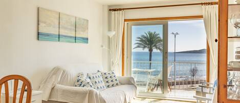 A room with a bed, a chair, a table, and a view of the sea.