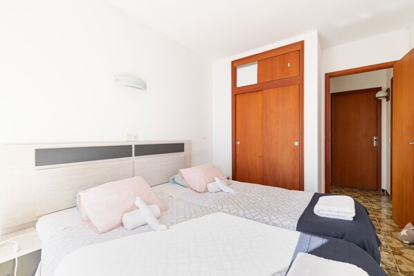 A hotel room with two beds, a wooden wardrobe, a bedside table, and a wall-mounted light fixture. - Skyline Cala Nau by Rentallorca (Cala Millor)