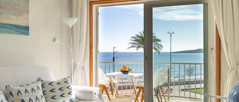 A room with a bed, a balcony with a table and chairs, and a view of the sea.