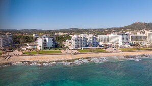 Et kysthotel med flere etager, en strand i forgrunden og et bjerglandskab i baggrunden.