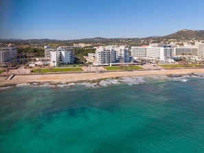 Ein Hotel an der Küste mit mehreren Etagen, ein Strand im Vordergrund und eine Bergkulisse.