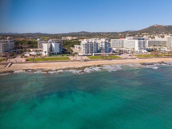 A coastal hotel with multiple floors, a beach in the foreground, and a mountainous backdrop. - Skyline Cala Nau by Rentallorca (Cala Millor)