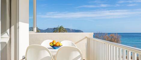 Un balcón con mesa y sillas, un frutero y vistas al mar y a las montañas.