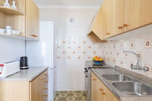 A kitchen with wooden cabinets, a white refrigerator, a toaster, a kettle, a sink, and a clock on the wall. - Skyline Cala Nau by Rentallorca (Cala Millor)