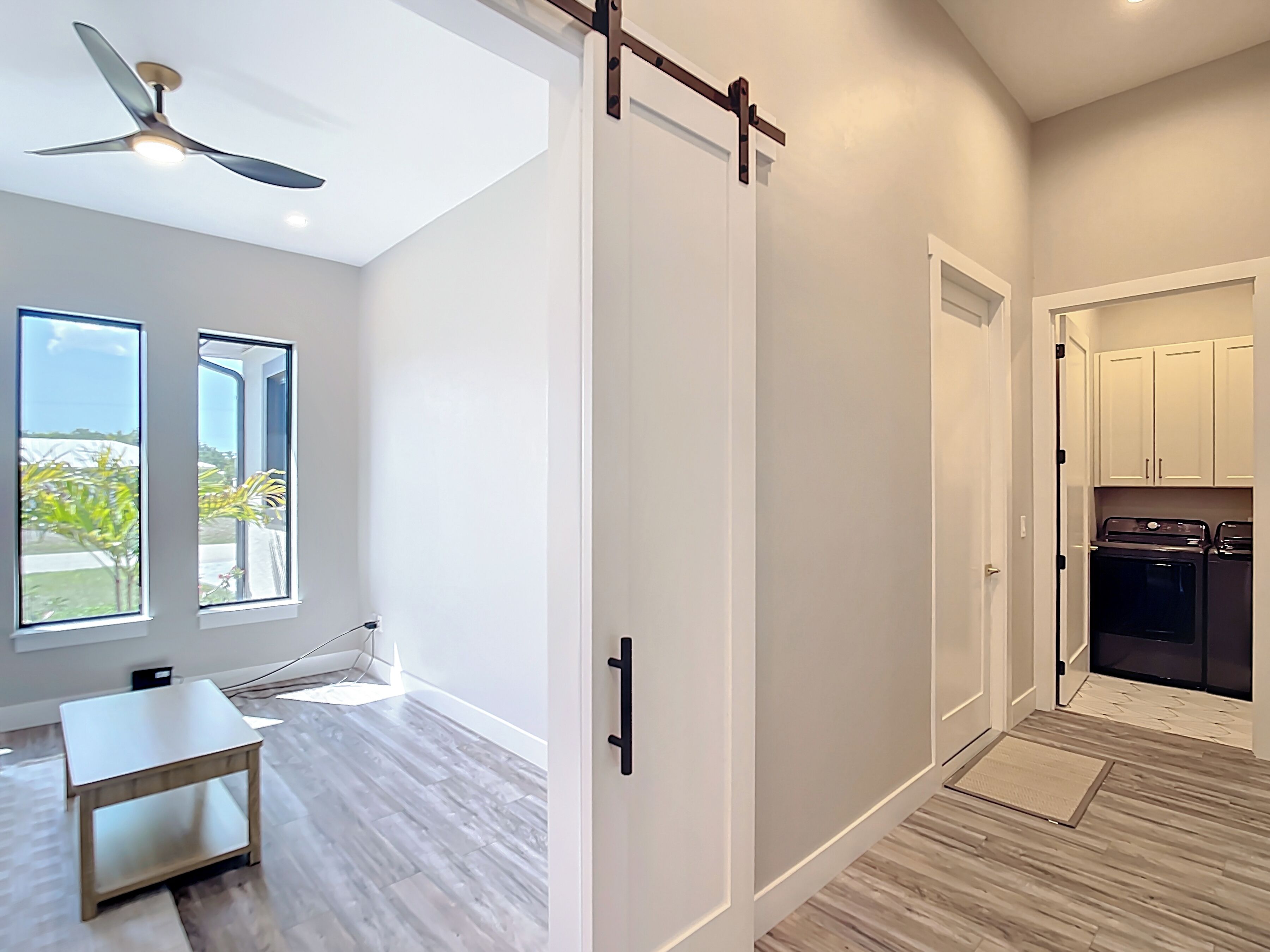 A modern interior with a sliding door, a ceiling fan, a dining table, and a view through a window.