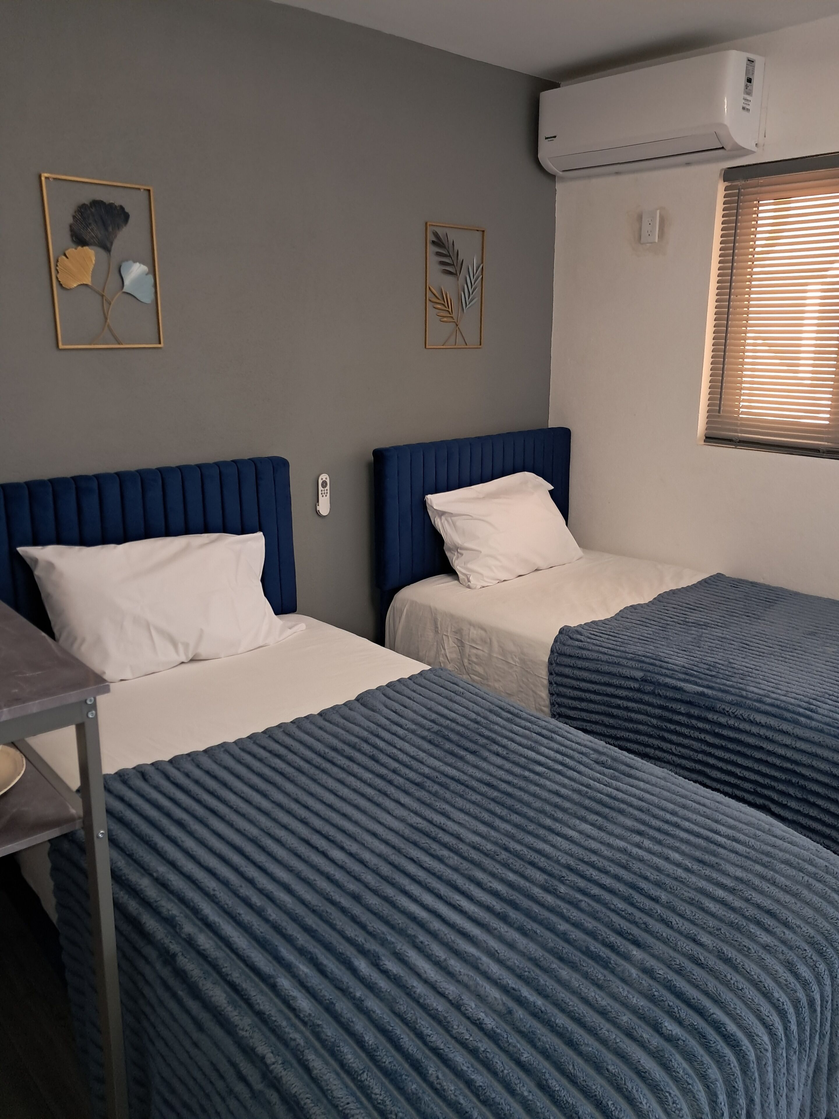 A room with two beds, a desk, and an air conditioning unit.