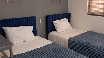 A room with two beds, a desk, and an air conditioning unit.