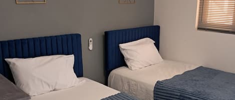 A room with two beds, a desk, and an air conditioning unit.