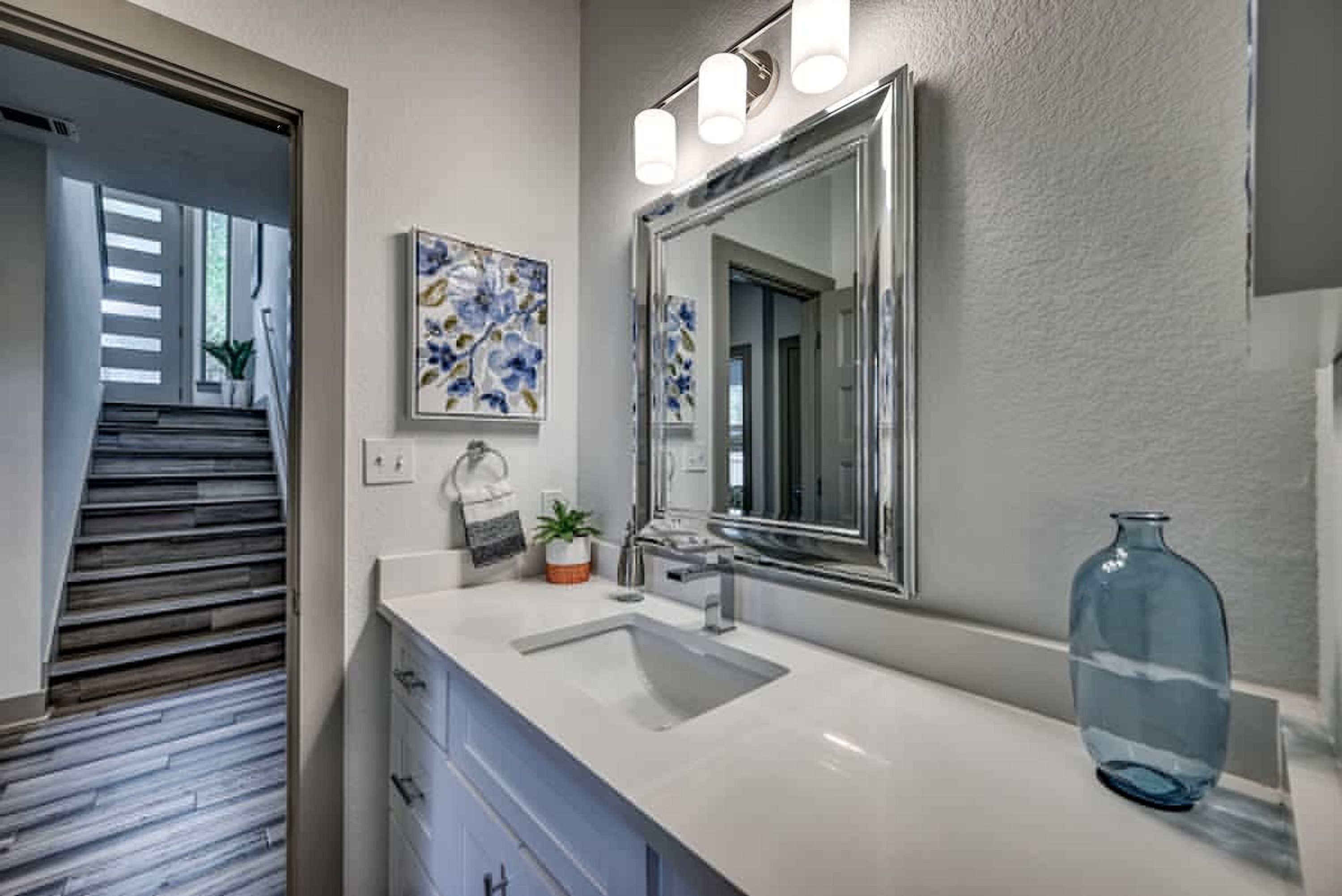 A bathroom with a white sink, a large mirror, and a blue vase.