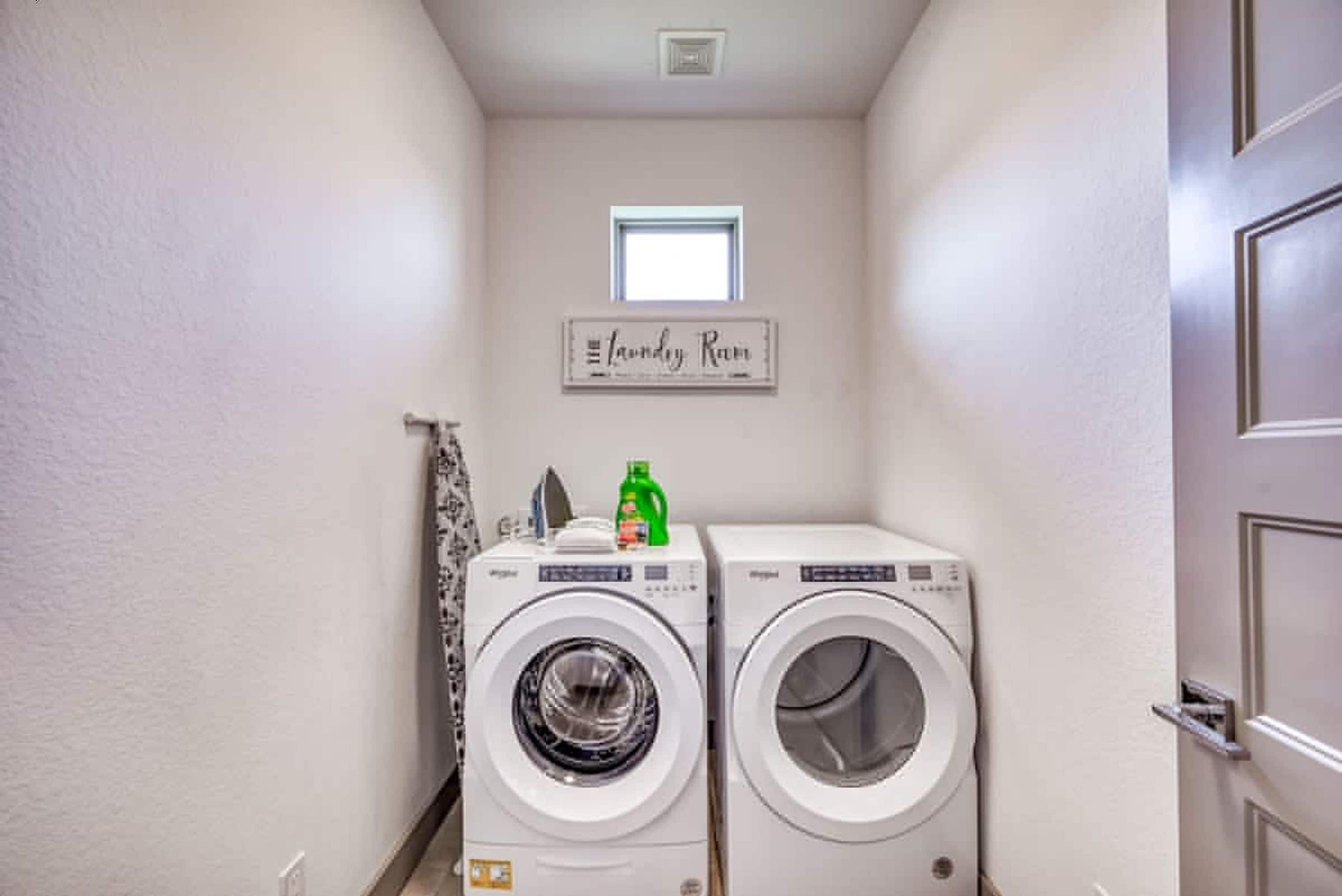A laundry room with two front-loading washing machines, a small window, and a sign above the machines.
