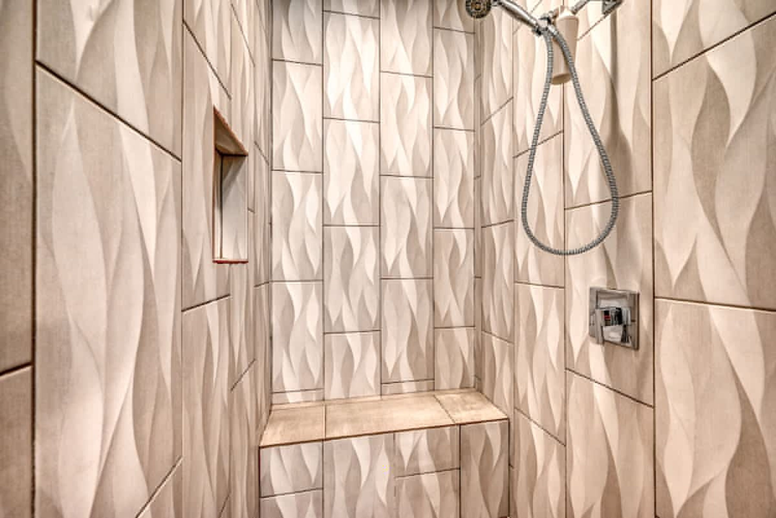 Eine Dusche mit geometrischem Fliesenmuster, einer Handbrause und einer Bedienkonsole.