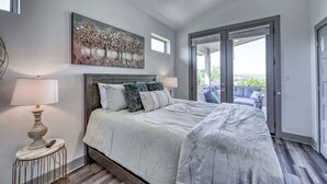 Ein Schlafzimmer mit Bett, einem Gemälde, einer Lampe und Blick durch eine Glastür.