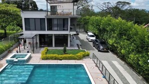 A modern two-story house with a swimming pool, a covered patio, and a car parked on the street. - Spectacular country house, in the coffee region, 5 minutes from the coffee park. (Armenia)