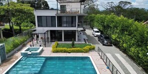 Una casa moderna de dos pisos con piscina, un patio cubierto y un coche estacionado en la calle.