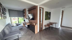 A modern living room with a sofa, a TV, a small table, and a herringbone-patterned floor. - Spectacular country house, in the coffee region, 5 minutes from the coffee park. (Armenia)