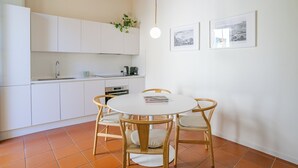 A kitchen with white cabinets, a round dining table with chairs, a hanging light, and two framed pictures on the wall. - Como Center Apartment Domus, Como, Italy (Como)