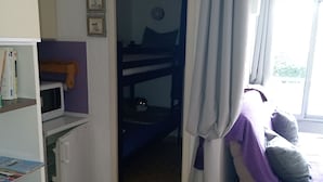 Une chambre avec un lit superposé, un bureau avec un ordinateur, une bibliothèque et une fenêtre avec des rideaux.