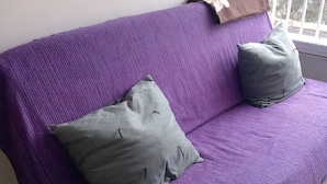 Un canapé violet avec deux coussins gris et un plaid marron.