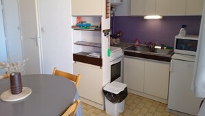 Une cuisine de taille réduite comprenant une table à manger, des chaises, une poubelle et un réfrigérateur.