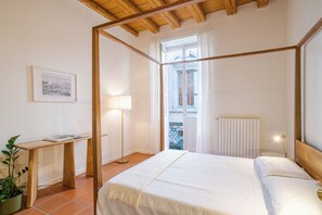 A bedroom with a four-poster bed, a bedside table with a lamp, a framed picture on the wall, and a view of the outside balcony. - Como Center Apartment Castrum, Como, Italy (Como)