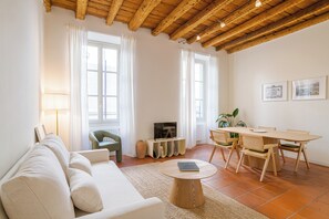 Ein geräumiges Wohnzimmer mit einer Couch, einem runden Couchtisch, einem Esstisch mit Stühlen und einem Fernseher.