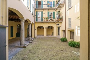 Ein Innenhof mit Steinboden, mehreren Balkonen mit Pflanzkübeln und einem zentralen, offenen Bereich.