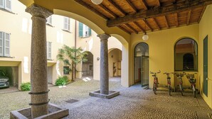 Ein Innenhof mit Säulen aus Stein, gefliestem Boden und Fahrrädern, die an der Wand lehnen.
