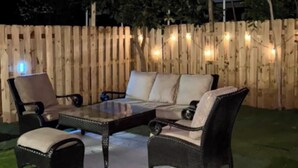 Un patio al aire libre con un toldo rojo, mobiliario de mimbre y luces colgantes.