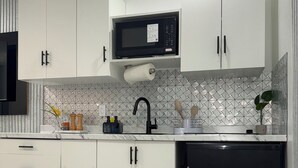 Una cocina moderna con armarios blancos, un microondas negro, un lavavajillas negro y un salpicadero de azulejos.
