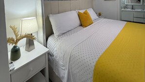 Un dormitorio con cama, mesita de noche, lámpara, ventilador de techo, un cuadro enmarcado y un espejo.