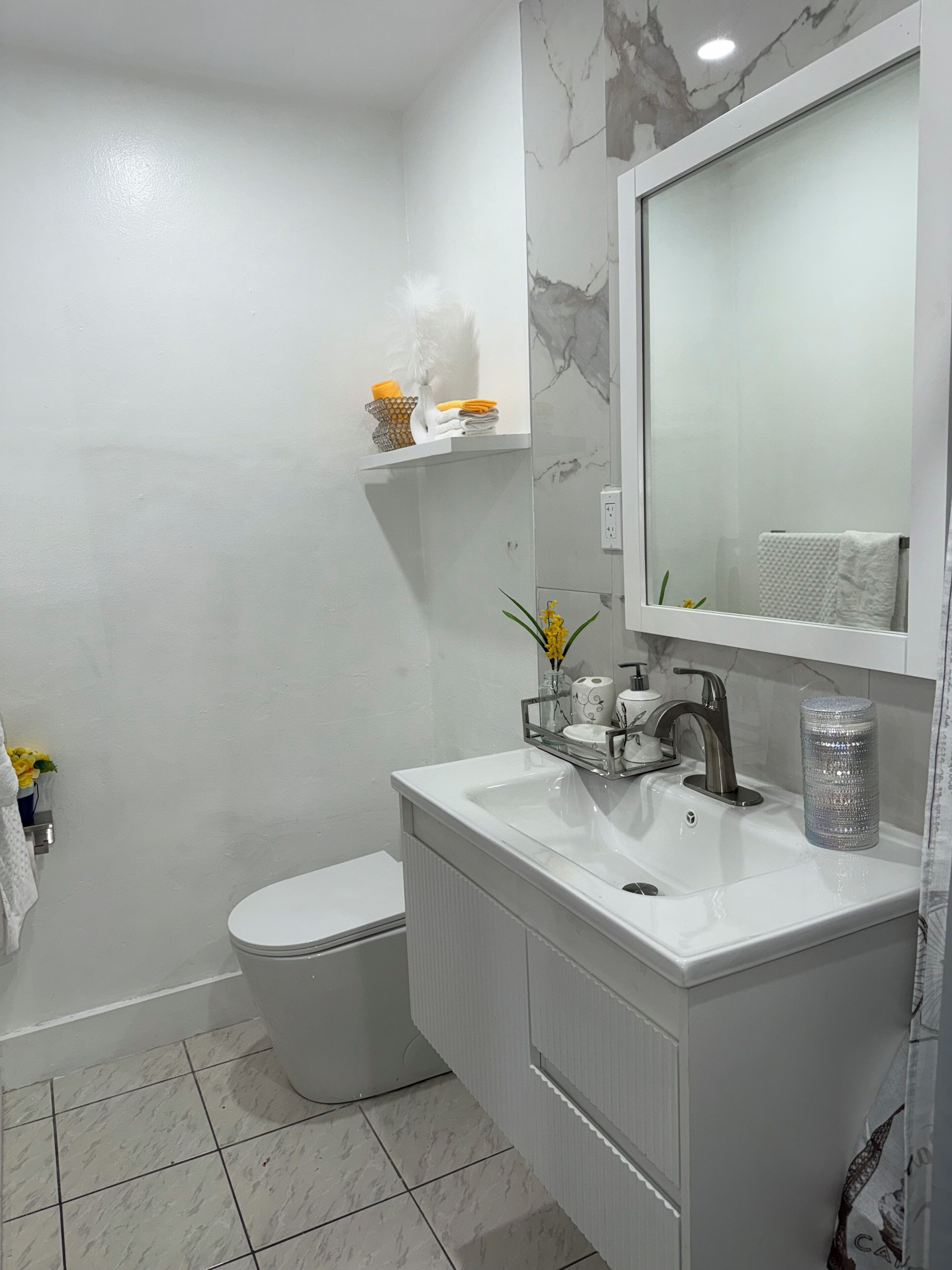 Un baño moderno con lavamanos, espejo y retrete blancos.