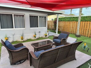 Een patio met rieten meubilair, een rode parasol en een houten omheining.