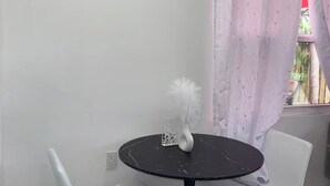 Una mesita pequeña y redonda, negra, con un florero blanco y un objeto blanco y mullido encima, junto a dos sillas blancas con asientos acolchados.