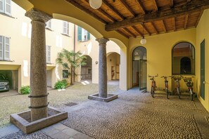 Ein Innenhof mit Säulen aus Stein, gefliestem Boden und Fahrrädern, die an der Wand lehnen.