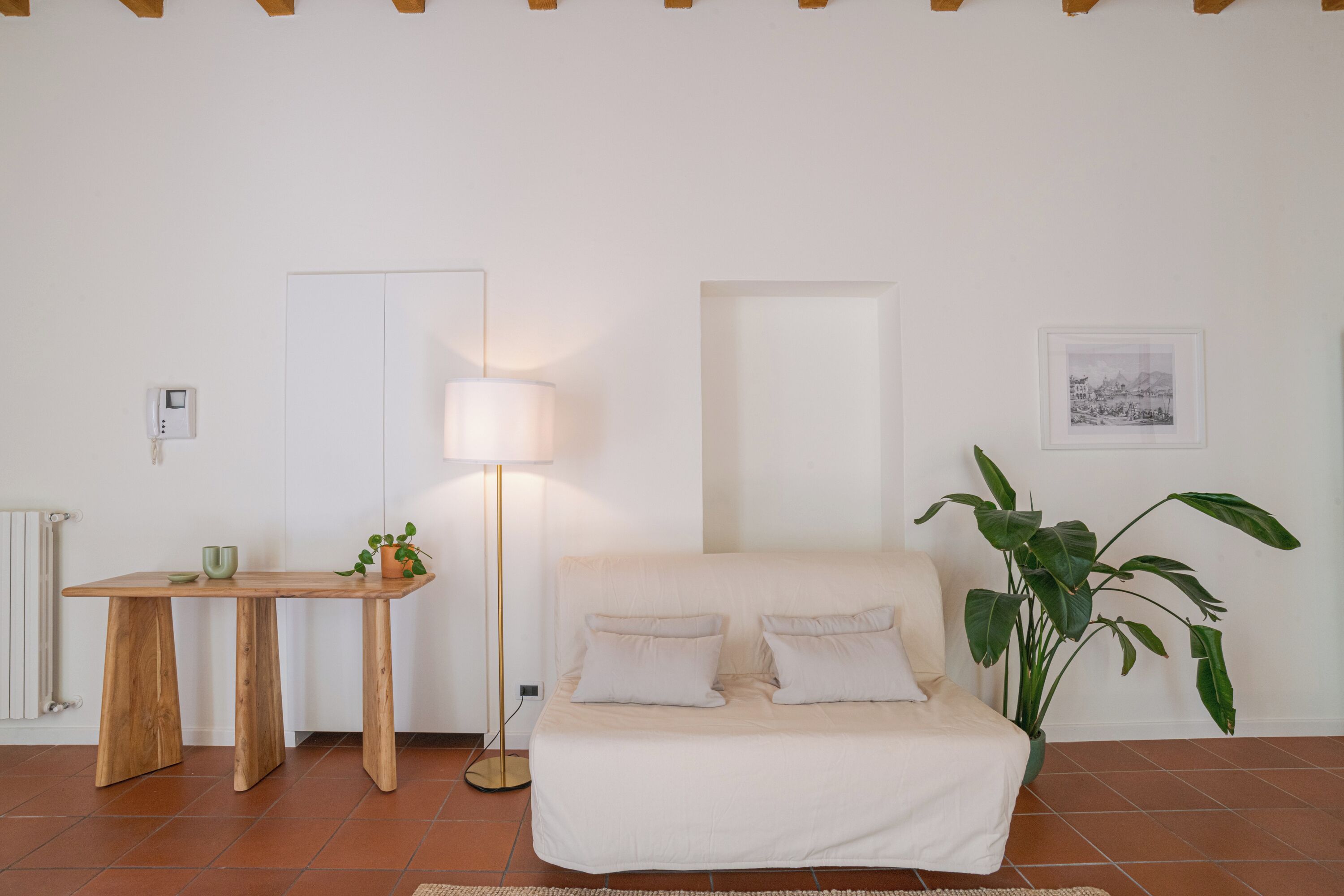 A room with a bed, a desk, a lamp, a plant, and a framed picture on the wall.