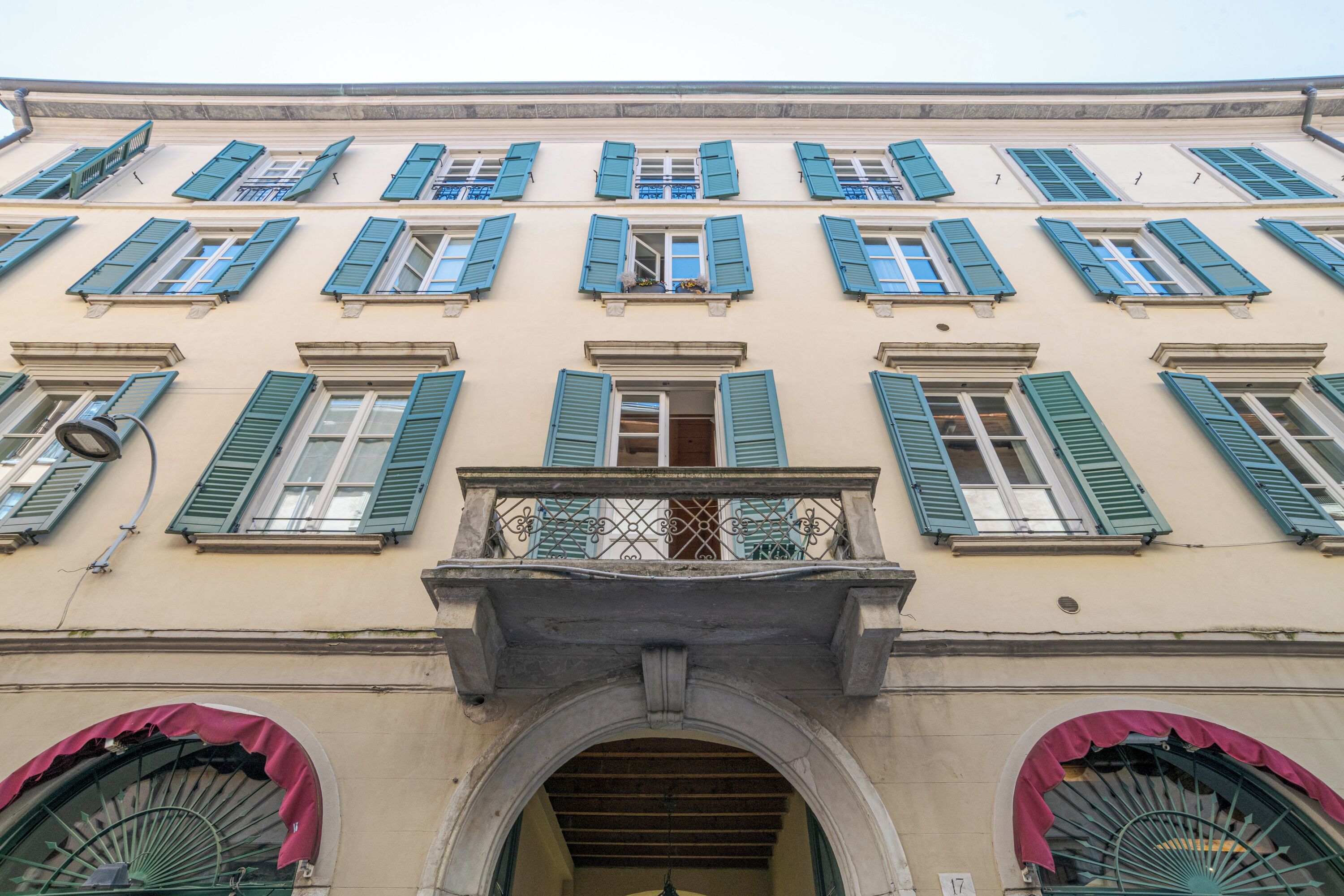 A building facade with multiple windows, a central entrance with an archway, and a balcony with a metal railing.