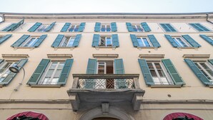 Une façade d’immeuble avec de nombreuses fenêtres, une entrée centrale surmontée d’un arc et un balcon doté d’une balustrade en métal.