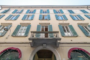Eine Gebäudefassade mit zahlreichen Fenstern, einem zentralen Eingang mit Bogen und einem Balkon mit Metallgeländer.