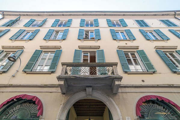 Fachada de edifício com várias janelas, entrada central em arco e varanda com guarda-corpo de metal.