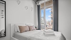 Un dormitorio moderno con un ventanal grande, una cama con ropa de cama blanca y arte mural geométrico.