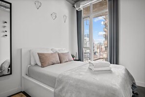 Ein modernes Schlafzimmer mit einem großen Fenster, einem Bett mit weißer Bettwäsche und geometrischer Wandkunst.