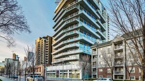 Un edificio de varios pisos con balcones, una acera y coches estacionados.