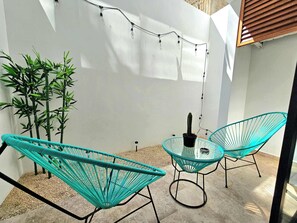 A small outdoor seating area with two turquoise chairs and a glass table, surrounded by a white wall and bamboo plants. - Downtown Studio, Oceanview Rooftop Pool & Gym (Playa del Carmen)