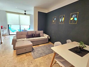 A modern living room with a sofa, a dining table, and a dark accent wall with framed artwork. - Downtown Studio, Oceanview Rooftop Pool & Gym (Playa del Carmen)