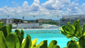 Ein Pool auf dem Dach mit freiem Blick auf umliegende Gebäude und einem teils bewölkten Himmel.