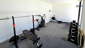 Ein Fitnessraum mit Squat-Rack, Langhantelbank, Kurzhanteln und einem Ergometer.
