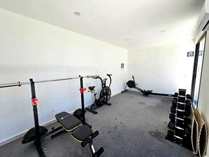 A gym with a squat rack, bench press, dumbbells, and an exercise bike. - Downtown Studio, Oceanview Rooftop Pool & Gym (Playa del Carmen)